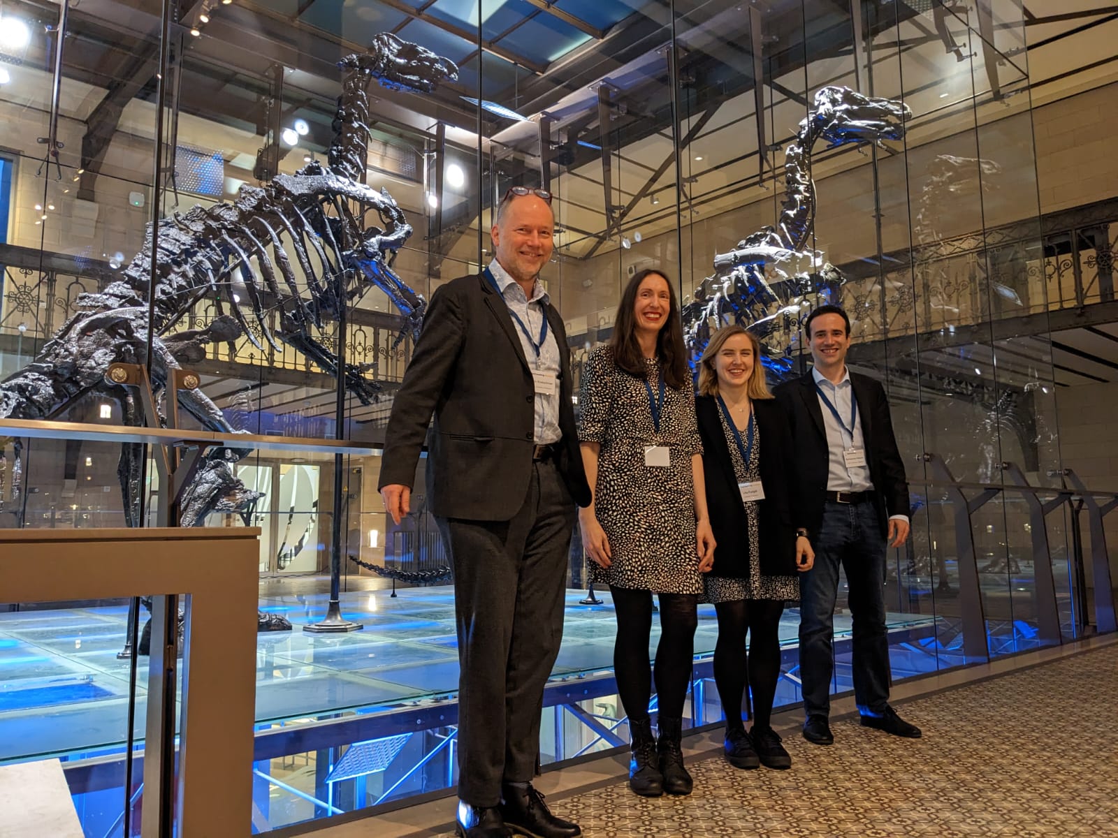 Four people standing in a row in front of a dinosaur skeleton exhibit.