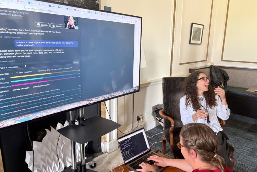 Post-conference gathering where participants play Kris’s game together. Abigail Rekas is playing, while Dr Sevra Guler Guzel can be seen laughing; the screen displays an AI agent character based on Dr Sevra Guler Guzel.